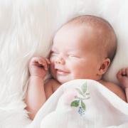 Sleeping newborn baby in a wrap on white blanket. Beautiful portrait of little child girl 7 days, one week old. Baby smiling in a dream..