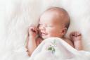Sleeping newborn baby in a wrap on white blanket. Beautiful portrait of little child girl 7 days, one week old. Baby smiling in a dream..