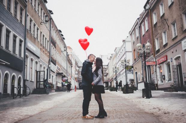 Denbighshire Free Press: A couple embracing on the street in front of heart balloons. Credit: Canva