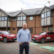 Jones Bros environmental manager Sam Higgitt pictured with the company's electric pool car fleet and in-front of the solar panels on the head office roof